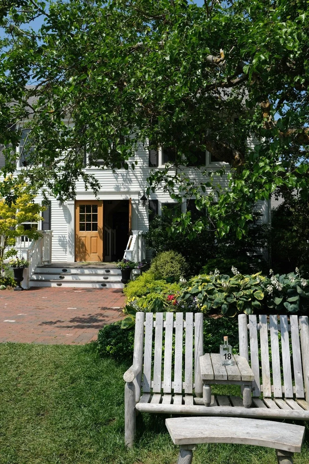 picture of a classic white two story house sitting behind a front porch with a pair of weathered wooden garden benches