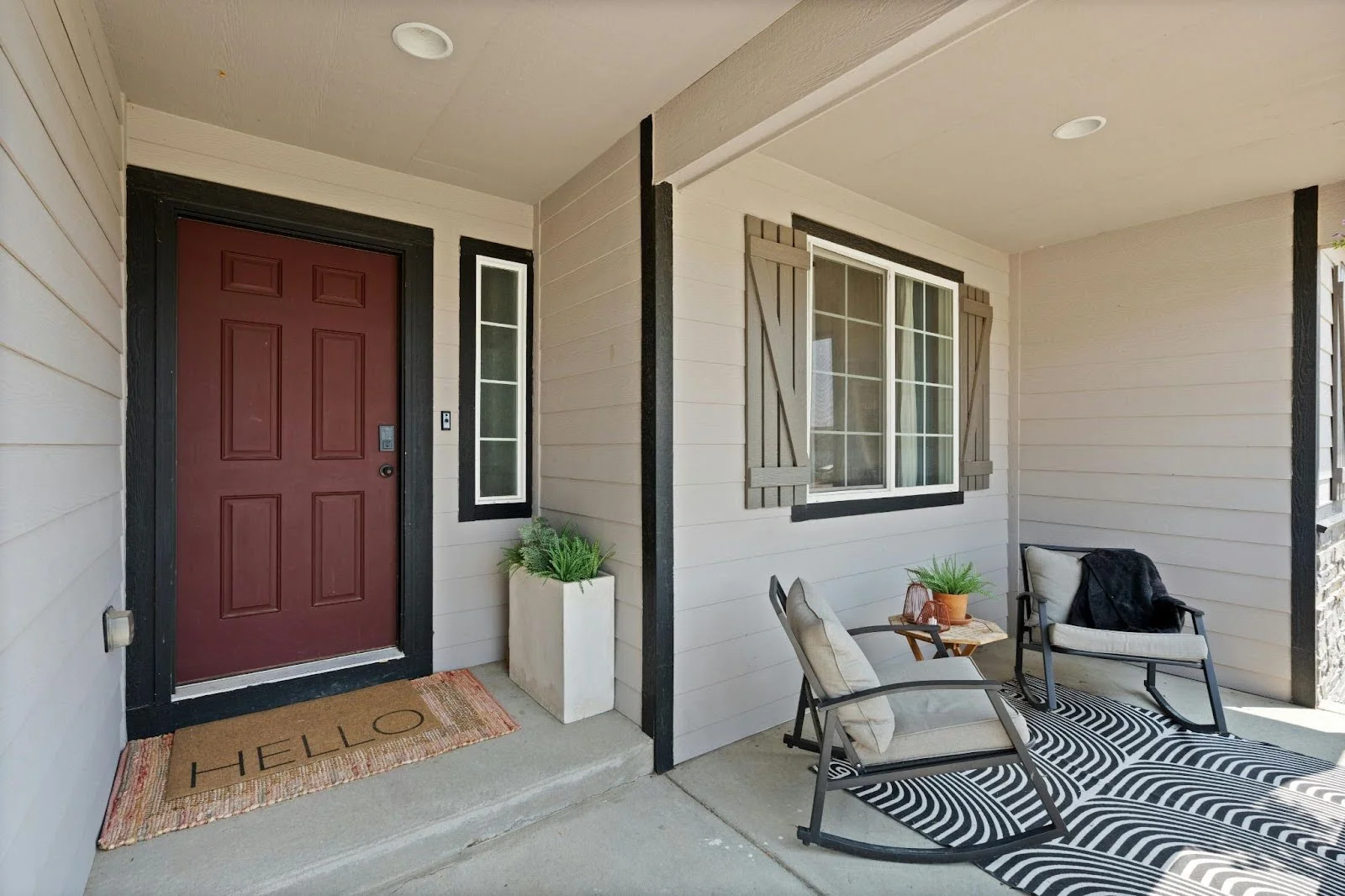 picture of a red wooden front door with black trim sitting next to a gray sided wall with a shuttered window