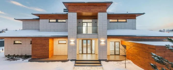 picture of a symmetrical modern two story house made with a home remodel checklist featuring stone and wood siding stands in a snowy landscape under a clear twilight sky