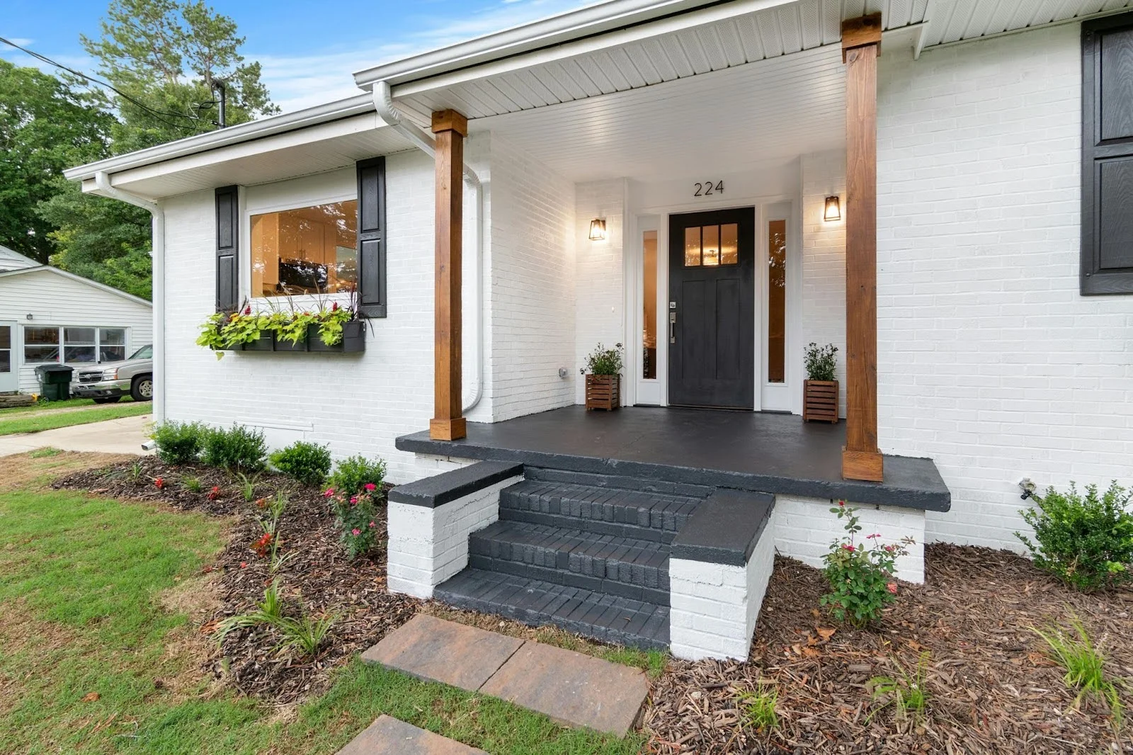 picture of a white brick home featuring a modern entryway with a dark gray porch matching stairs a black front door with glass panes and two wood support columns