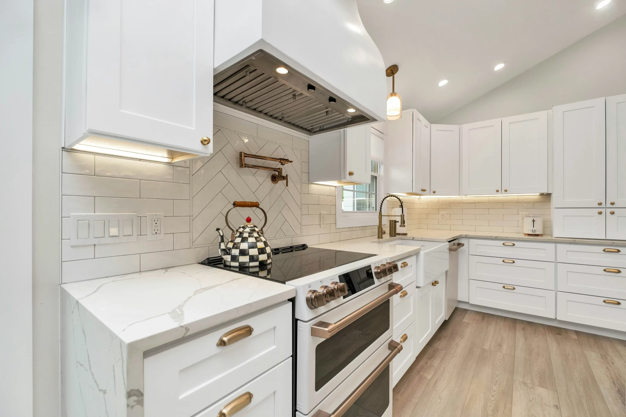 photo of a white kitchen with wood flooring white cabinets and brass fixtures against a white tile kitchen backdrop