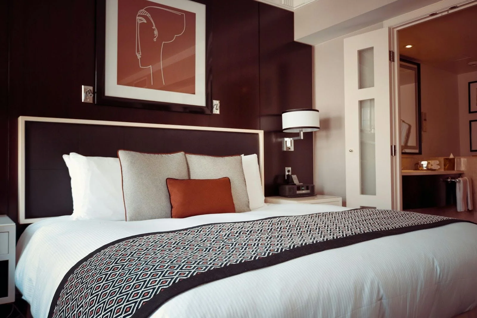 picture of a luxurious master bedroom featuring a large bed with patterned linens and dark wood wall paneling with integrated artwork