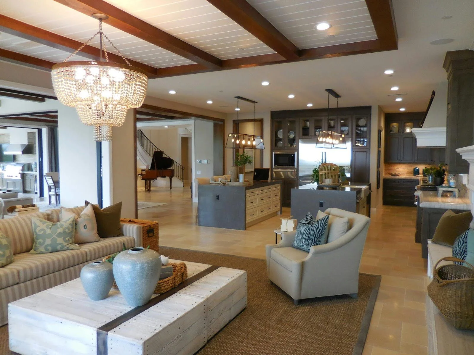 picture of a warm open concept living area with a beaded chandelier neutral sofas and a view into a kitchen with dark cabinetry