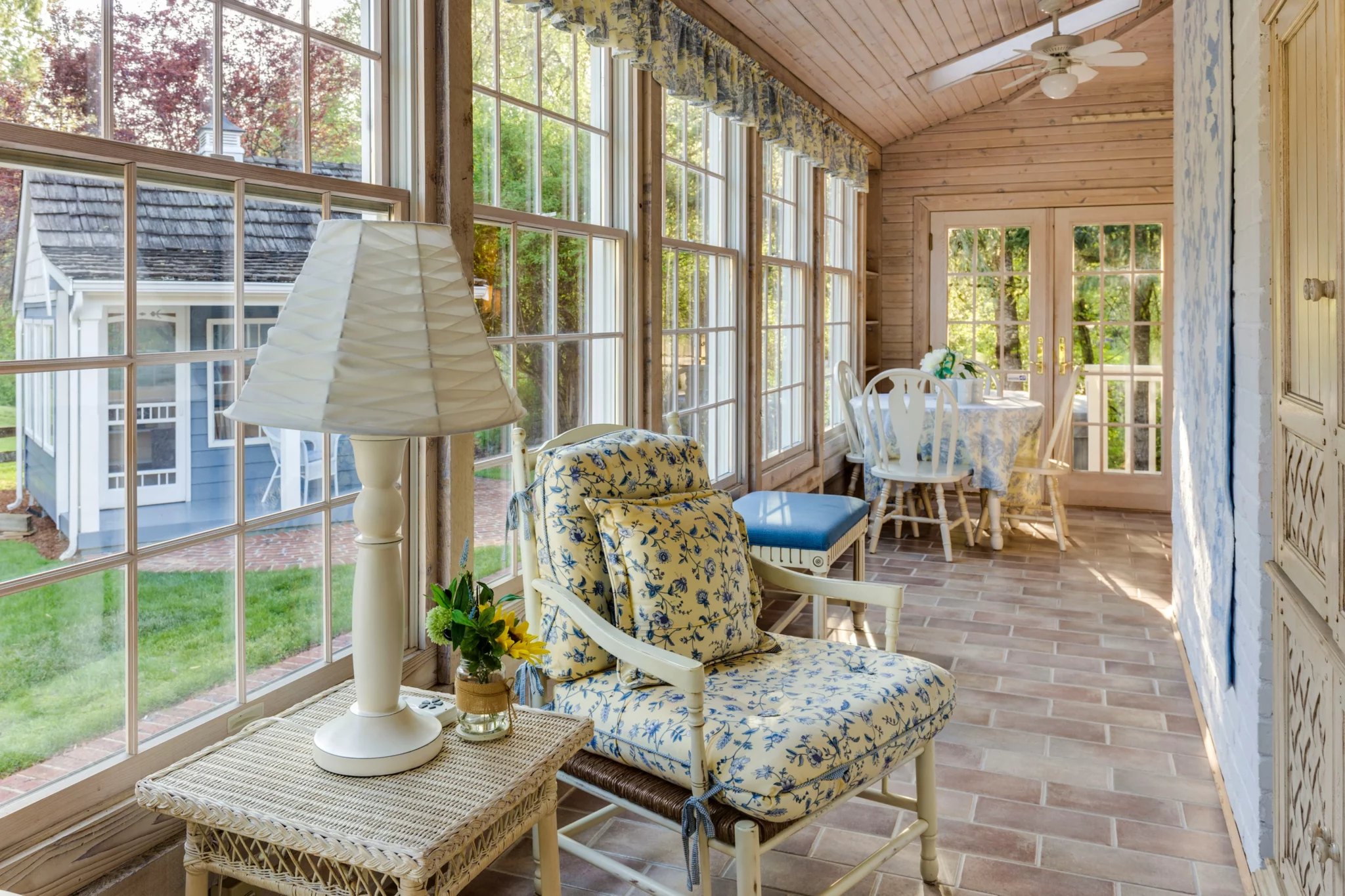 photo of a bright porch addition room with brick floors vintage furniture and windows