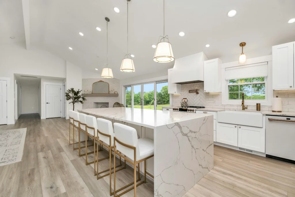 photo of a bright modern white kitchen with white granite countertops and a large granite kitchen island with white and gold chairs in Long Beach CA