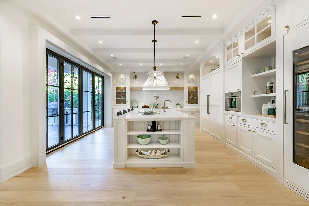 Modern Room addition Los Angeles featuring a bright white kitchen with a large island, custom cabinetry, light wood floors, and black-framed glass doors opening to the patio